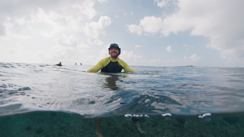 Surfer waits the wave. Underwater splitted view of the happy male surfer sitting in the ocean and waiting the wave