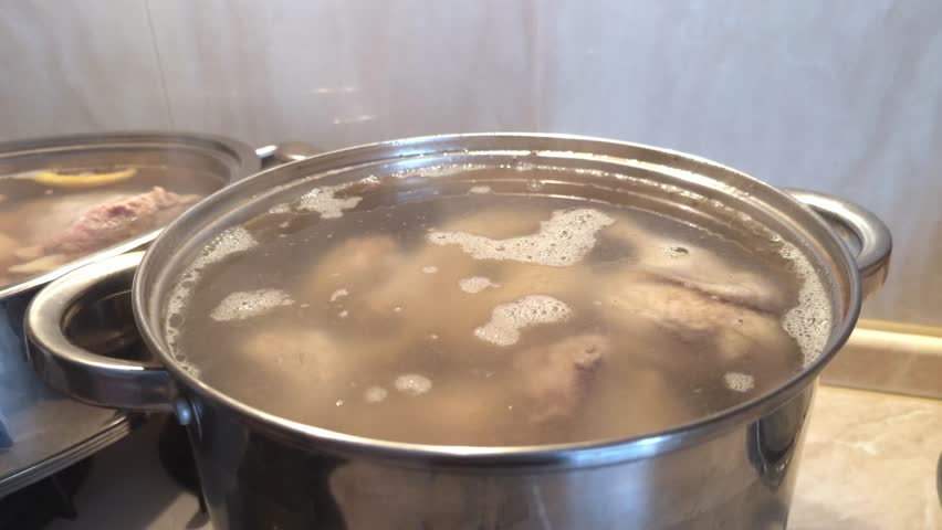 Boiling meat broth in a large pot on the stove, homemade soup cooking