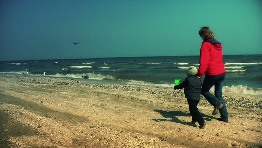 Mother and little boy running on the beach, scaring seagulls, slow motion