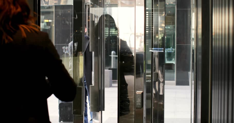 Woman turning door, pulling blue suitcase, man leaving business, speech bubbles floating over glass. Revolving, lobby, entrance, professionals, corporate, urban, luggage