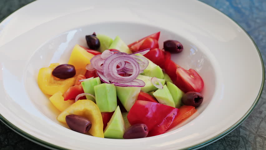 Fresh Greek salad served in a white plate with cucumbers, tomatoes, bell peppers, red onion rings, and Kalamata olives