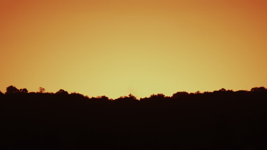 A peaceful view of an orange yellow sky above dark silhouetted hills during sunset