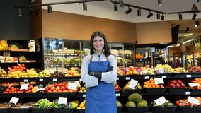 Portrait of a beautiful young female worker smiling at the camera with her arms crossed, standing proudly in front of a fruit and vegetable section inside a modern grocery store - Powered by Shutterstock - Get 15% off with code: PIKWIZARD15
