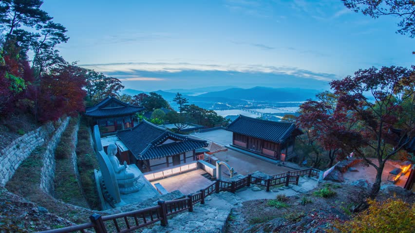 Sujongja Temple sits atop a hill amidst a forest of autumn leaves, offering views of Buddha statues and traditional Korean buildings in Namyangju, Gyeonggi Province, South Korea. Timelapse Zoom out.