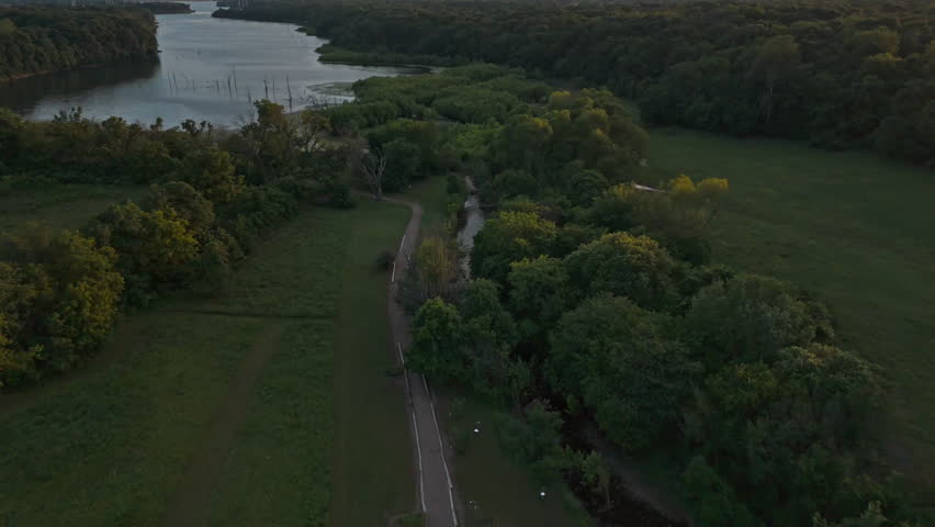 Drone pullback of dense green forest canopy with small lake inlet visible beyond the treetops