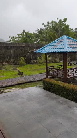 Rainy outdoor scene with a wooden gazebo and lush green garden, creating a peaceful and calming atmosphere