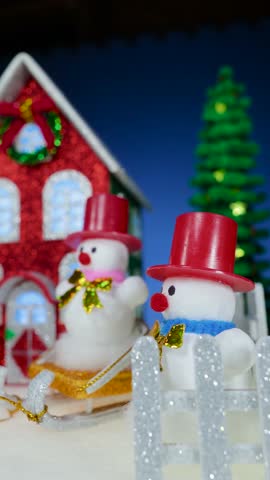 Near the red house there are glass Christmas trees and snowmen with and without sleds