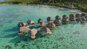 Moorea island resort featuring overwater bungalows connected by wooden walkways, sitting on a turquoise lagoon with clear shallow water, surrounded by lush green mountains - Powered by Shutterstock - Get 15% off with code: PIKWIZARD15