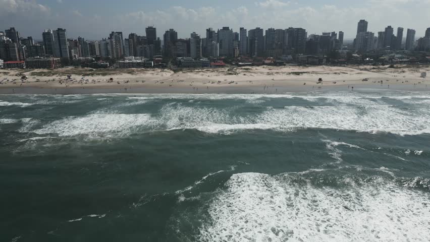 A dynamic aerial sweep over crashing waves approaching Torres’ sandy shoreline with the skyline shimmering in the distance.