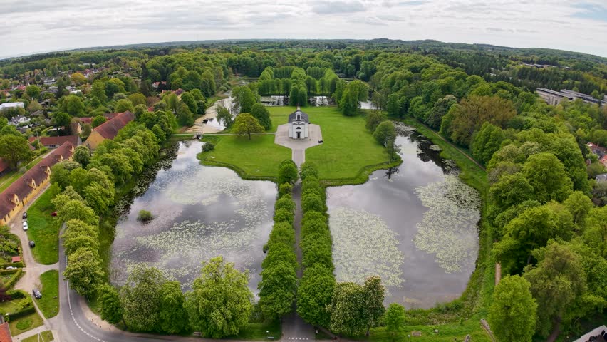 Top‑down aerial of a formal garden layout with twin reflective ponds lined by leafy trees, central walkway and a small monument surrounded by lilies.