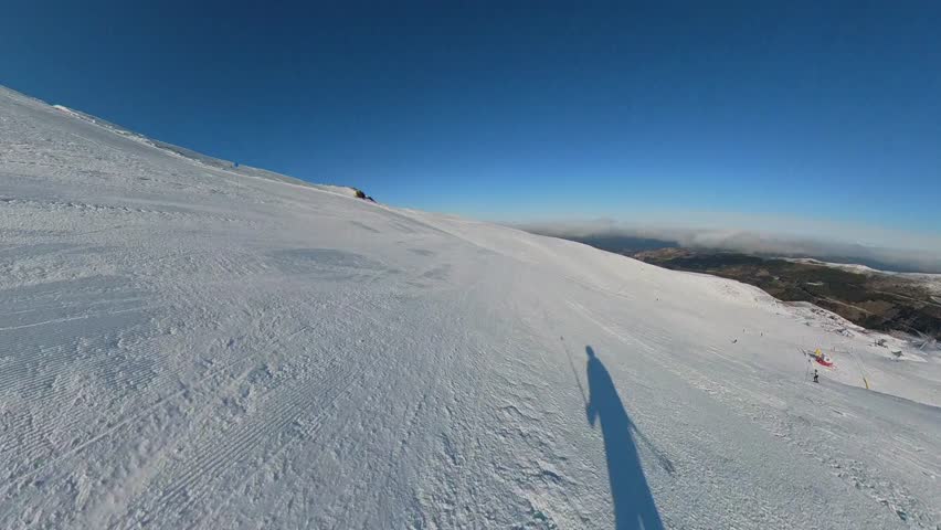 4K action camera POV skiing on a wide, intermediate blue-level slope in Sierra Nevada, Granada, Spain, showcasing a smooth, controlled descent under a pristine blue sky.