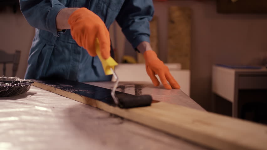 Man painting wooden surface in black paint using painting roller