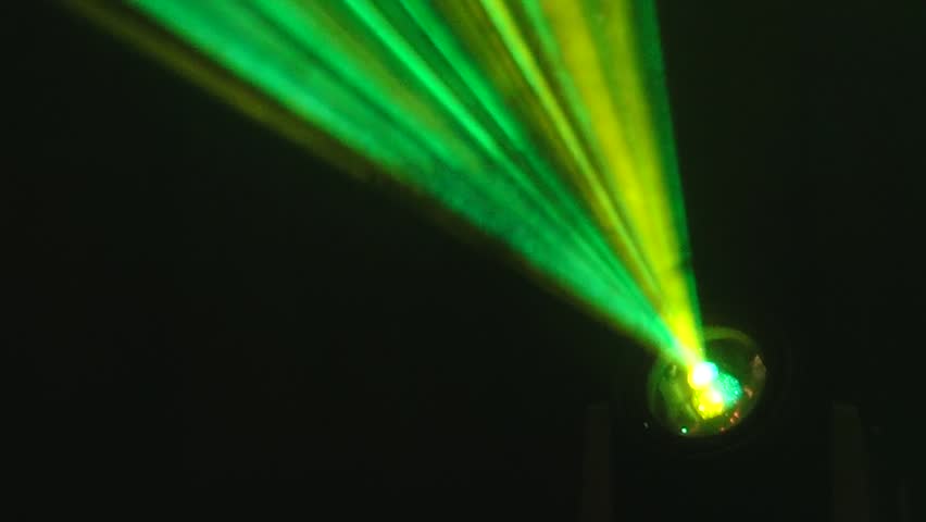 Vivid green and yellow laser beams project from a stage spotlight in a dark environment, creating a dramatic lighting effect with ample copy space.