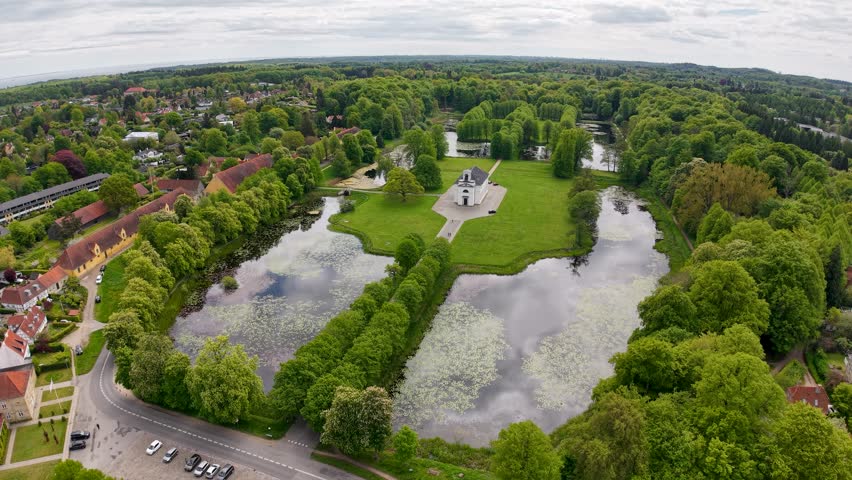 Drone aerial footage capturing geometric rectangular ponds and water channels surrounded by lush green countryside and trees in Denmark.