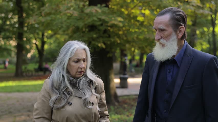 Calm and beautiful grandfather and grandmother walking in a green area and talking to each other.