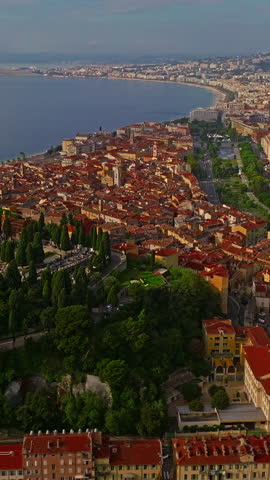  Aerial view of bustling beachfront promenade on sunny day. Beautiful panorama in Nice, France. Palm trees, old houses in old town azure sea and green hills. Summer in French Riviera