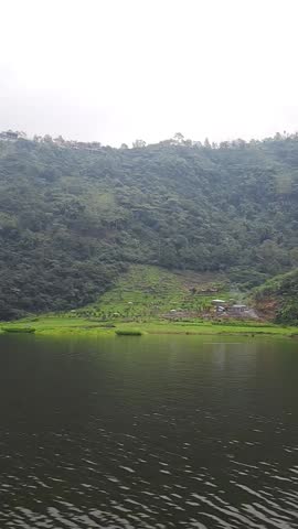 Serene high-altitude lake in the Indonesian highlands, surrounded by lush green forest and hills under a peaceful, cloud-covered sky. Telaga Menjer, Wonosobo, Indonesia. 03 June 2025.