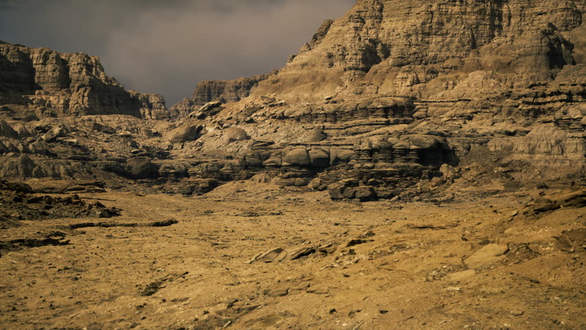 A vast rocky desert landscape showcases dramatic formations and a dry terrain. The surroundings reveal a mixture of textures, highlighting the rugged beauty of nature.