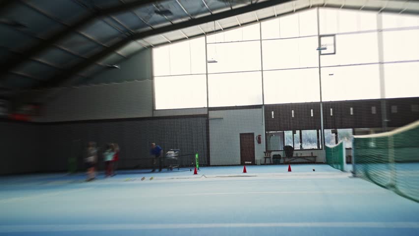 player sprinting across blue indoor court, sharp lateral footwork drills and reactive practice, coach tossing balls for quickness, high tempo agility focus, sneakers kicking up dust