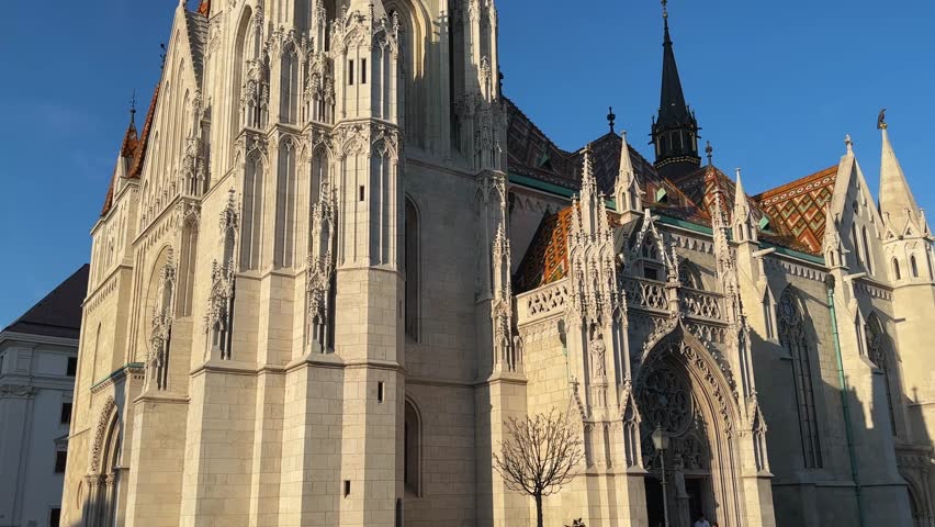 Tower in the main facade and south facade of Gothic Matthias Church of the 14th century in Budapest, bottom view close-up while vertical panning against the clear sky
