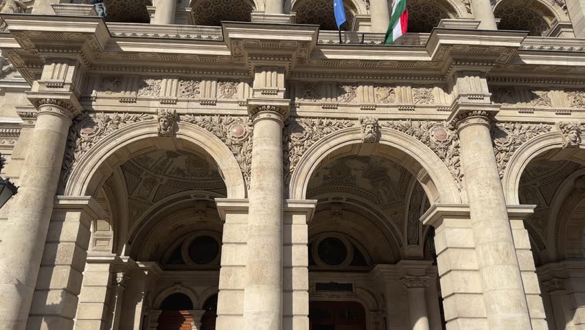 Upper part of main facade of the Hungarian State Opera House of 19th century with arched portico in Budapest, Hungary, bottom-up view while vertical panning at sunny day 
