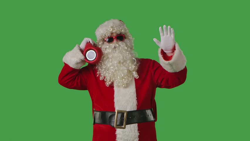 Santa Claus dancing cheerfully with a portable speaker on a green chroma key background