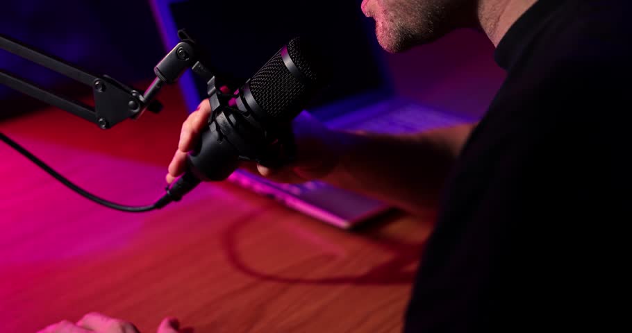 man talking in microphone in broadcasting studio with neon lights. podcast recording, streaming