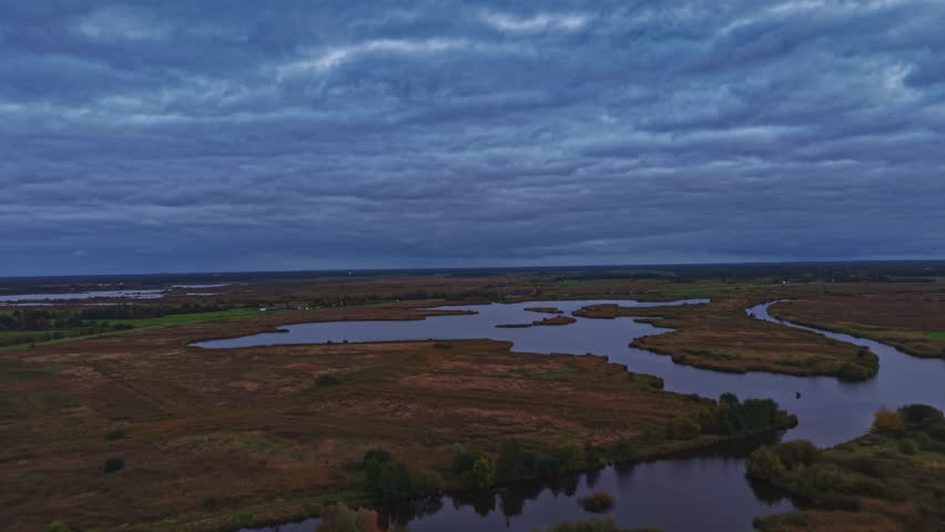 Soft clouds drift lazily over a vast landscape where a river winds through expansive wetlands, creating a peaceful scene as dusk settles in.