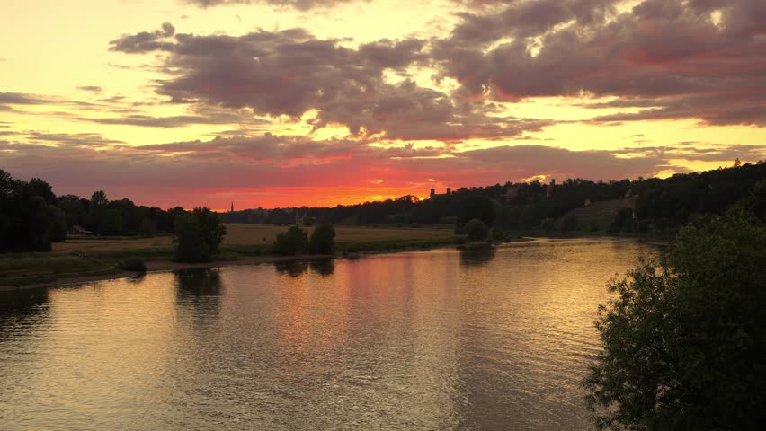 Summer sunset over slowly flowing Elbe River along green meadows, with silhouettes of Dresden historic castles. Ideal for travel, nature, tourism,scenic landscape footage.
