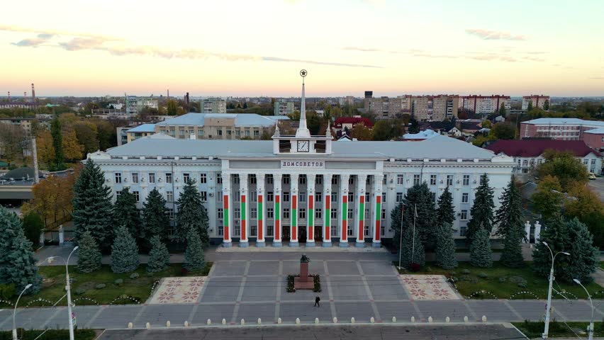 Aerial view of the House of Soviets, the Tiraspol city hall building, featuring classical soviet architecture and flags of Transnistria, with a statue of Lenin in the main square