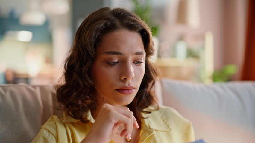 Anxious woman browsing smartphone message sitting home couch closeup. Sad brunette reading disturbing cellphone message feeling troubled. Concerned lady watching banking app worried financial problem.