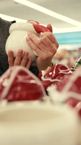 Close-up of a girls hand holding an interesting white and red mug in a store as she makes her choice.