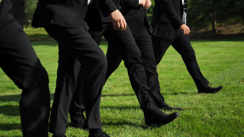 Group of men in a black pants and shoes walking on the green lawn grass in the park