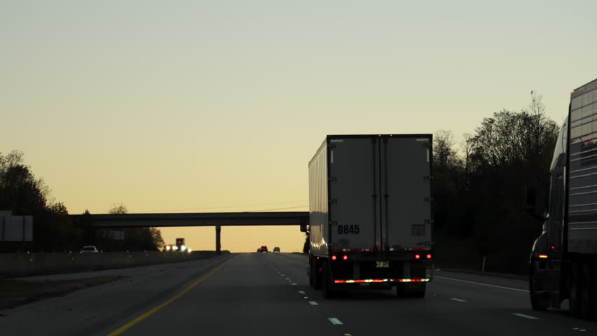 Semi-trucks with 53-foot dry van semi-trailer are traveling on a highway under the bridge at golden sunset. long-haul freight transportation on an American interstate.