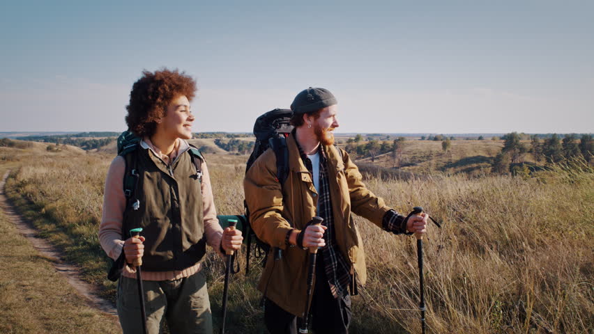 Red bearded man with black girlfriend engages walking at autumn countryside slow motion. Young sportive family hikes on hilly rural site on sunny day