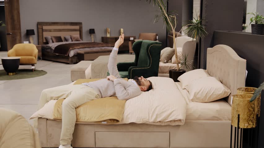 Adult man lying on a bed, giving a thumbs up, satisfied with the comfort in a modern furniture showroom