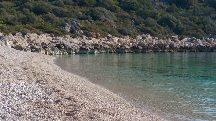 Calm turquoise water gently lapping a secluded pebble beach. Crystal-clear turquoise water gently laps the shore of a secluded pebble beach, nestled against a backdrop of lush green vegetation