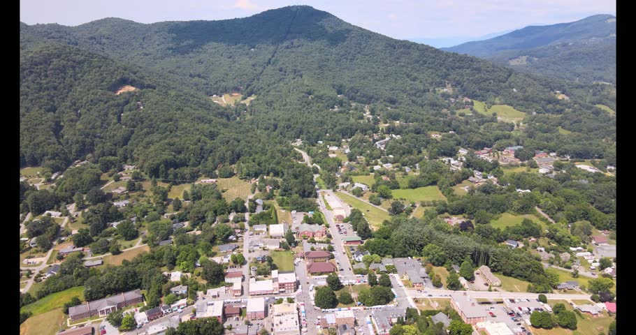 Aerial 4K drone view of downtown Burnsville, North Carolina in summer during a craft fair, showing vendor tents, town streets, and surrounding Blue Ridge Mountain scenery.