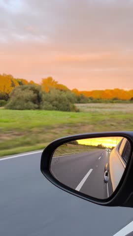 A beautiful road. The sunset reflected in the side mirror of a car on the highway.