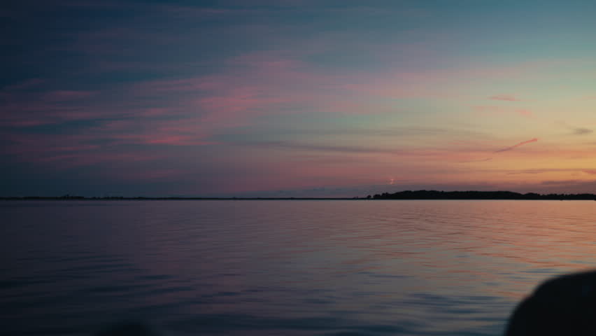 A serene ocean view at sunset, with soft pastel colors reflecting across calm water and a distant shoreline.