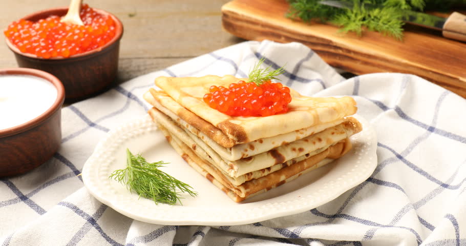 Tasty crepes with red caviar, dill and sour cream on wooden table, closeup