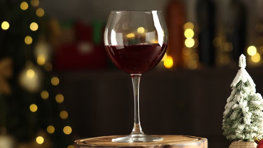 Glass of red wine on table against blurred lights, rotating. Christmas and New Year celebration