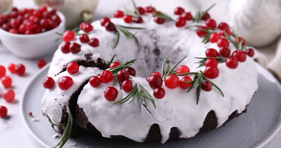 Woman taking piece of tasty Christmas cake with cranberries and rosemary at table, closeup