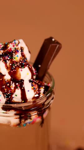Close-up of cherry gently placed atop creamy chocolate milkshake with whipped cream and sprinkles