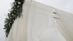 A close-up of a wedding arch decorated with white flowers, greenery, and draped fabrics that flow gently in the wind - Powered by Shutterstock - Get 15% off with code: PIKWIZARD15
