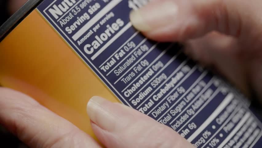 A woman holds a canned food item and highlights its high sodium content on the nutrition label, emphasizing health awareness and informed food choices.