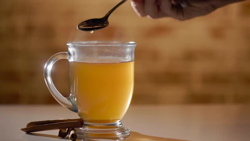 Slow-motion footage of honey being poured into a steaming cup of tea, capturing a cozy beverage moment, natural sweetness, and relaxing kitchen atmosphere.