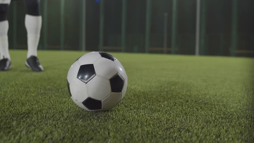 Low-section shot of an athlete wearing cleats kicking a soccer ball on green grass, highlighting sports action, energy, and outdoor activity.