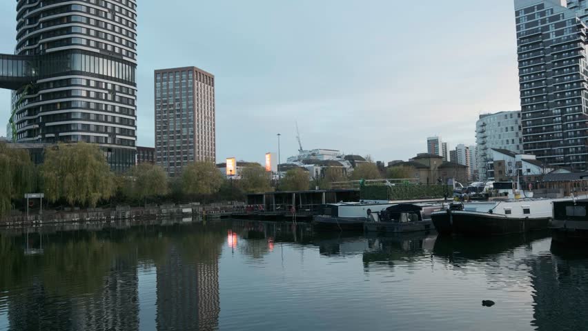 Smooth panning shot revealing a modern urban marina filled with moored houseboats and yachts, set against a backdrop of contemporary residential skyscrapers and office buildings at dusk