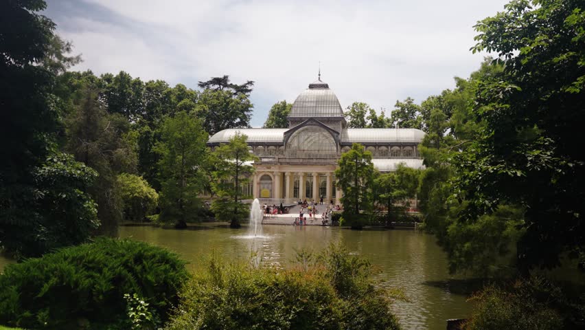 The Palacio de Cristal overlooks a calm lake surrounded by lush summer greenery in Madrid